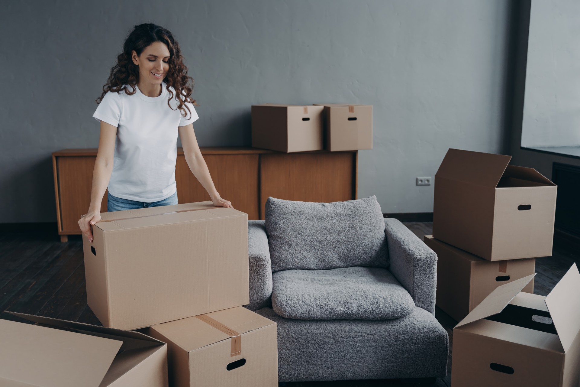 Smiling woman lifting a box with ease, in the midst of an orderly move.