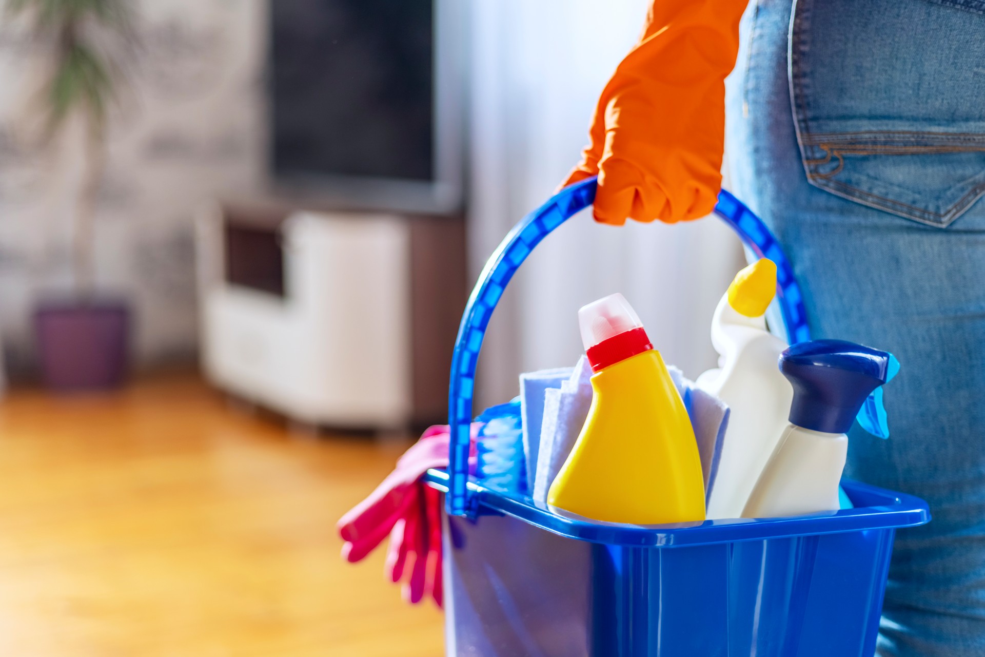 Woman in rubber gloves with bucket of cleaning supplies ready to clean up